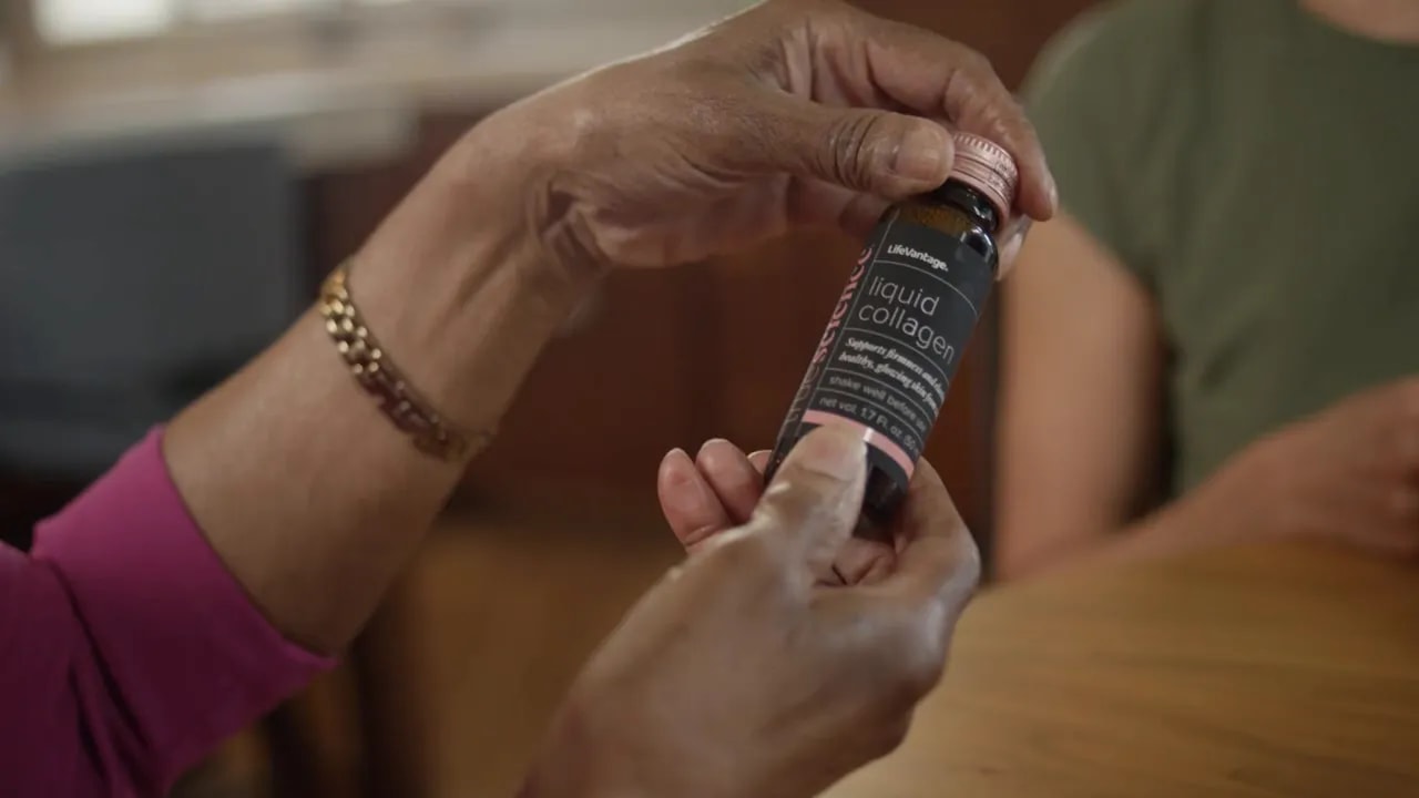 Handen die een fles LifeVantage True Science Liquid Collagen vasthouden met het productlabel.